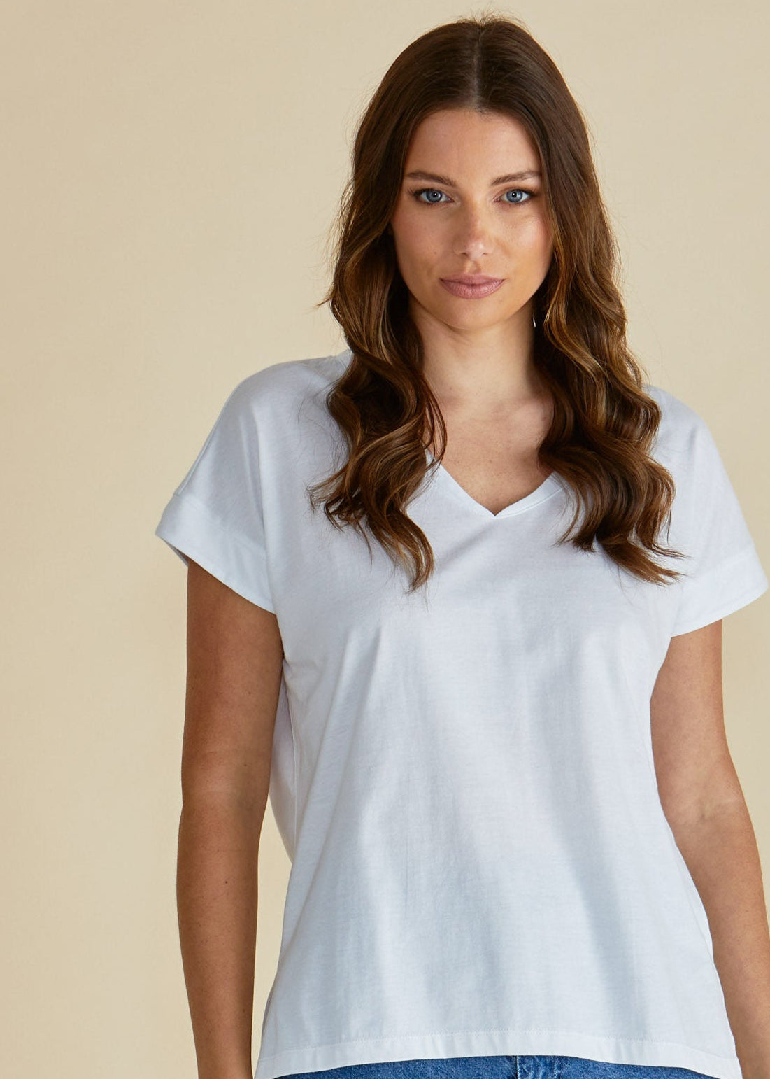 Woman wearing a white t-shirt and blue jeans against a beige background